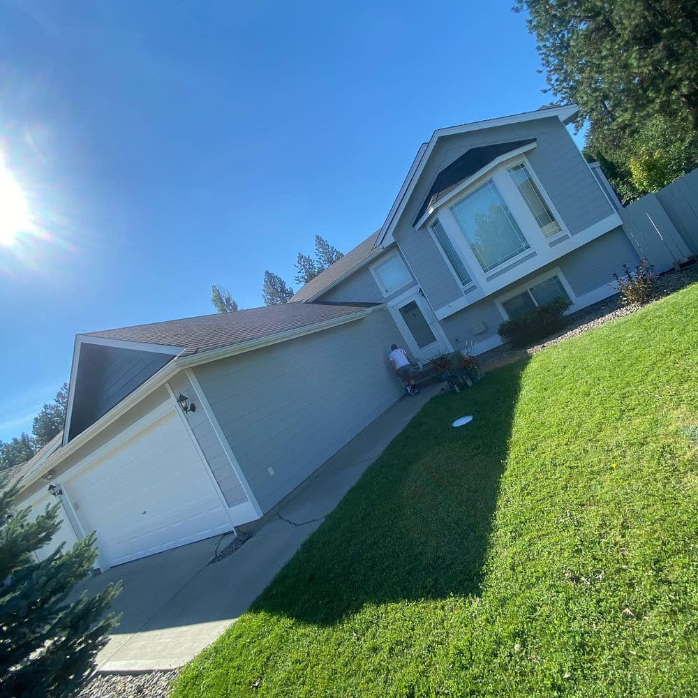 Modern gray house with manicured lawn and driveway under clear blue sky.