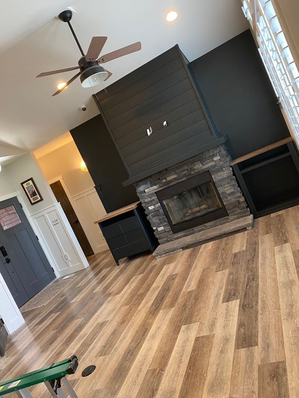 Living room with modern stone fireplace, wood flooring, and ceiling fan, featuring black accent wall.