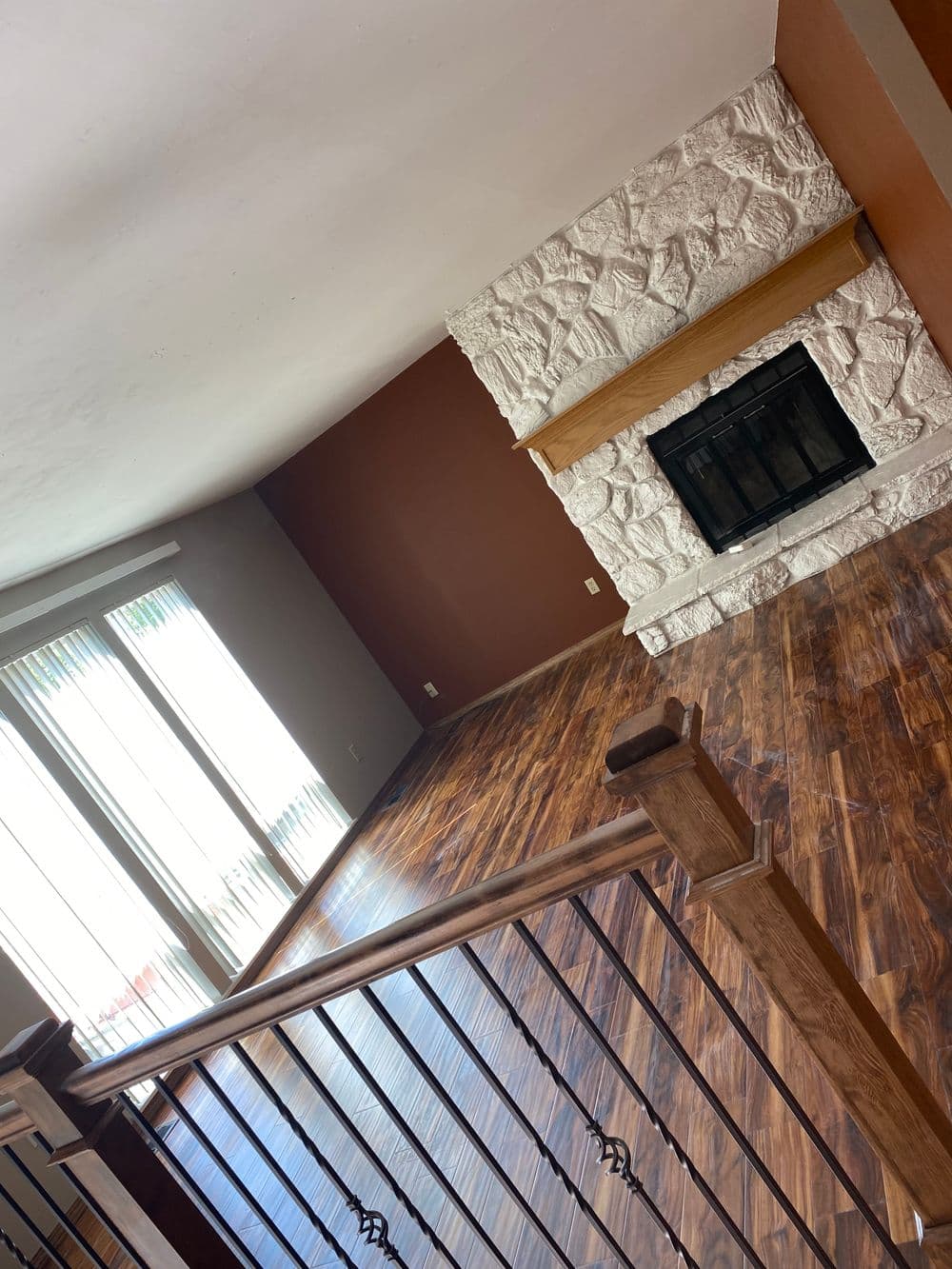 Spacious living room with wooden flooring and stone fireplace, featuring large windows.