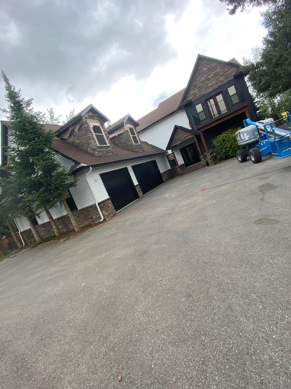 Modern two-story house with a mix of stone and wood, garage, and construction lift in the driveway.