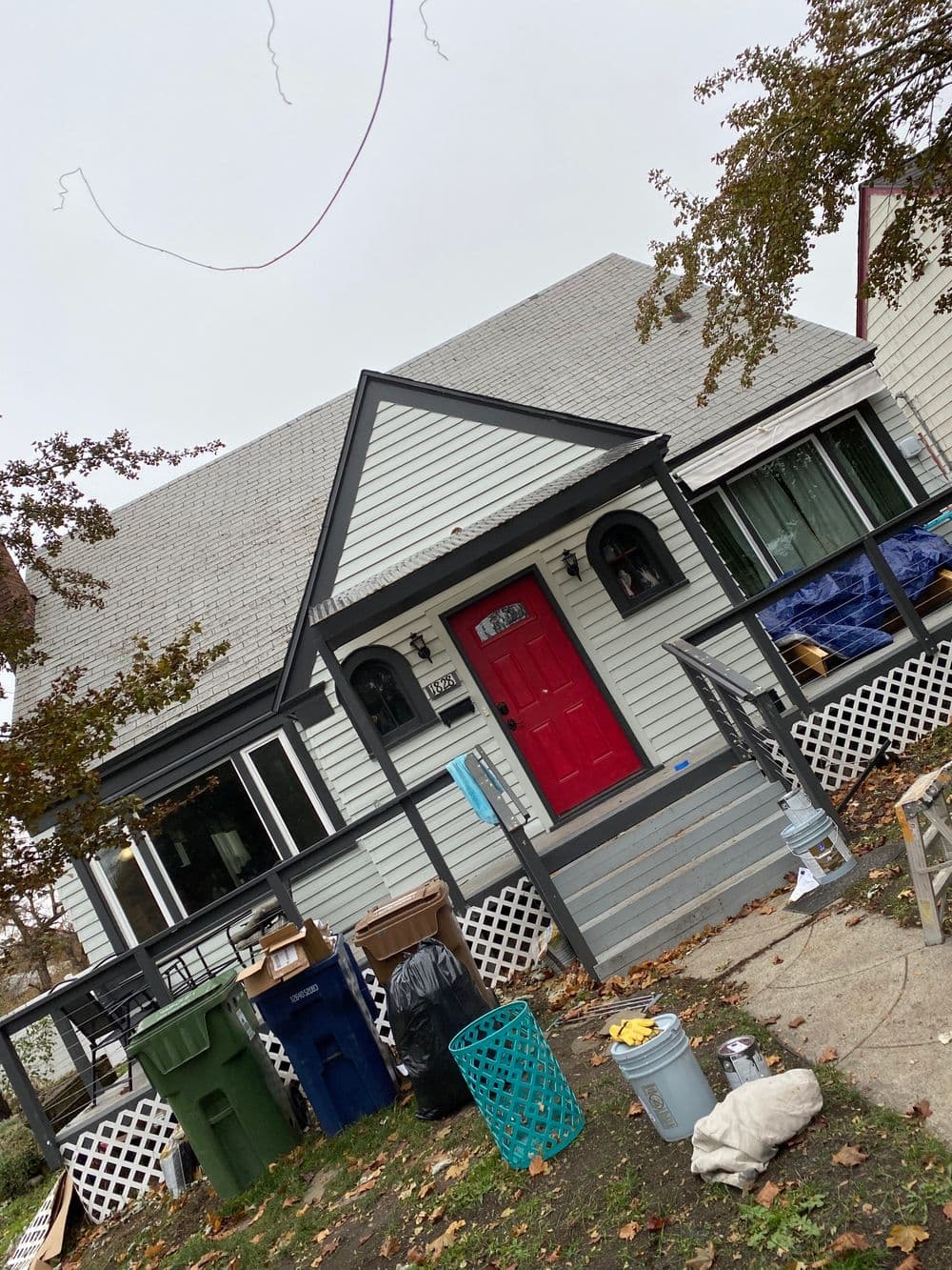 Charming house with a red door, front porch, and yard clutter in fall setting.