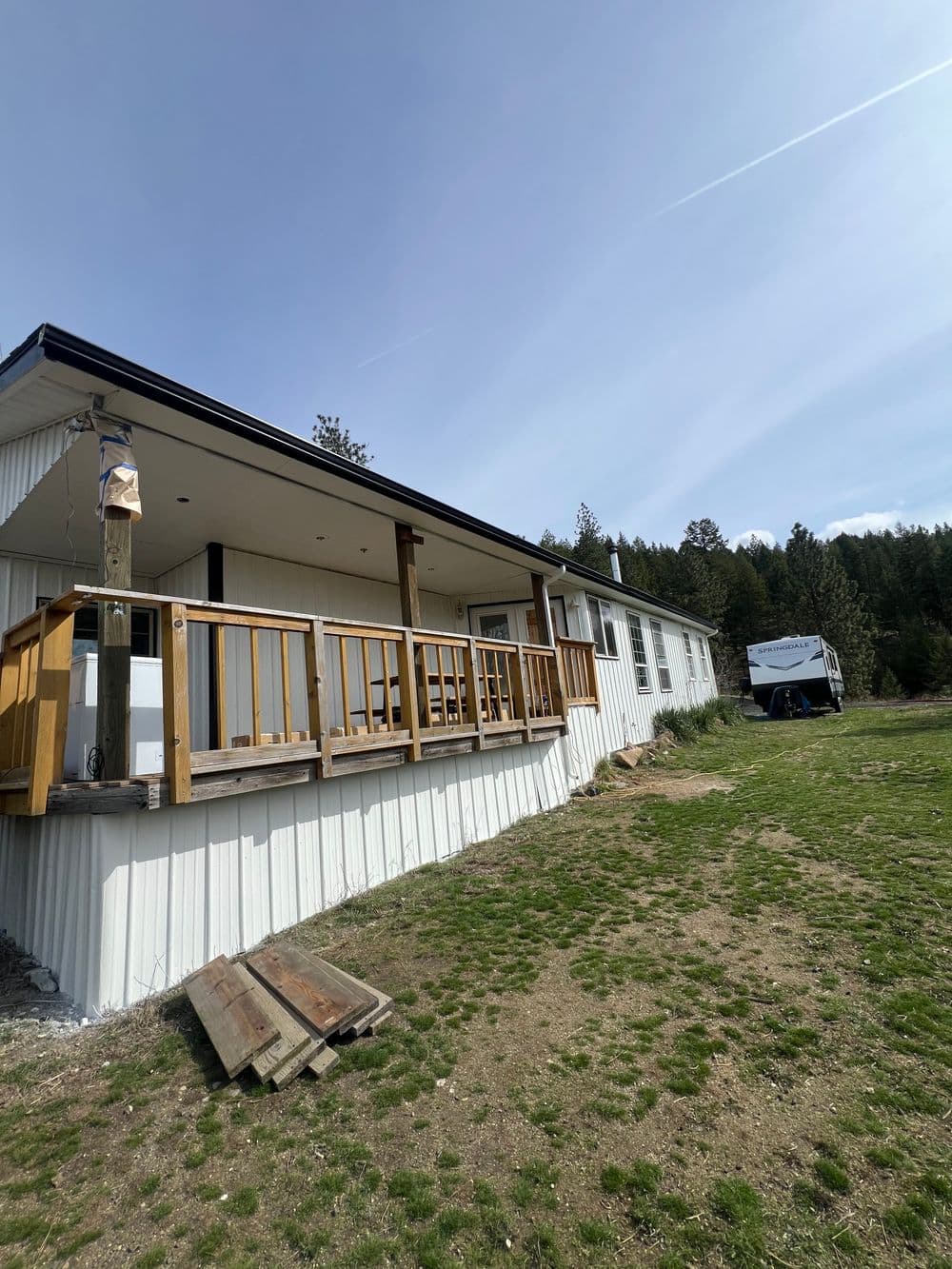 Single-story mobile home with wooden porch and scenic green landscape in the background.
