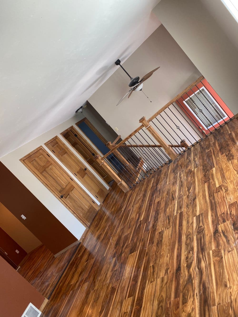 Spacious modern living room with wood floors and wooden railing, featuring ceiling fan and doors.