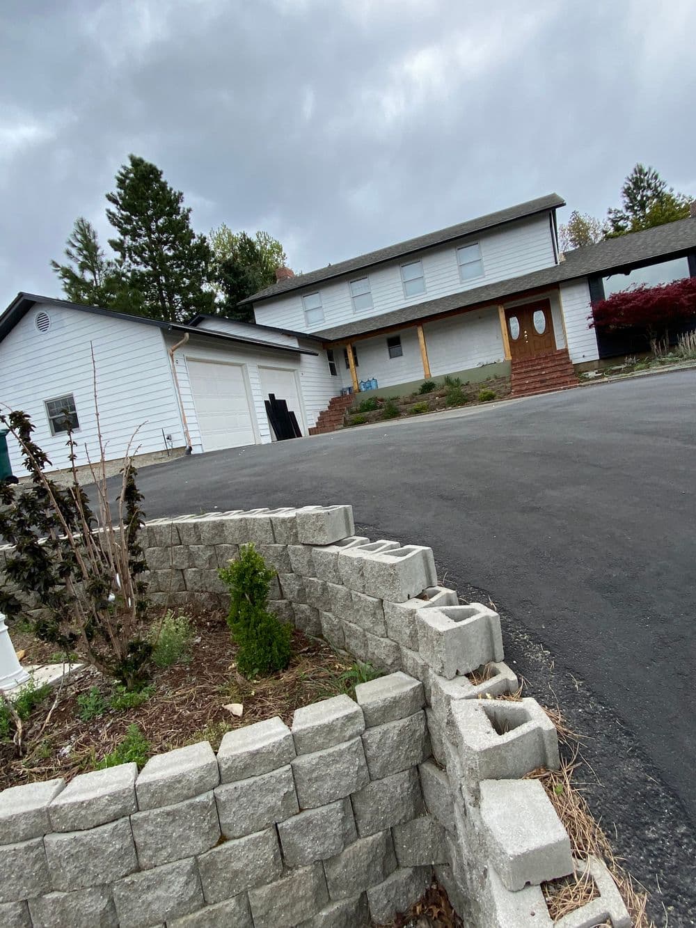 Two-story white house with a driveway and landscape stone wall under a cloudy sky.