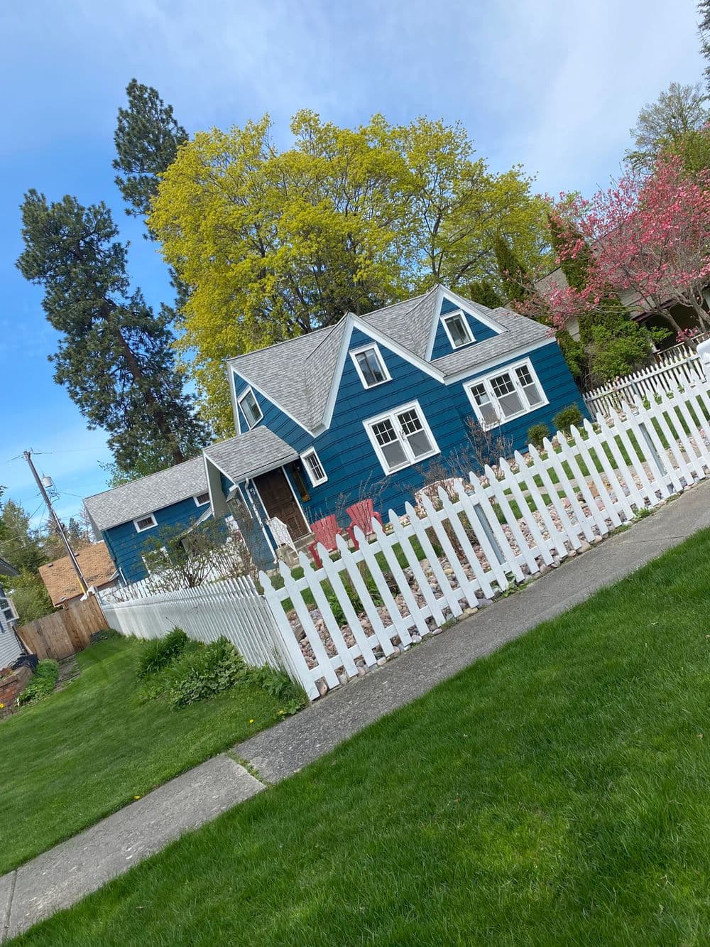Charming blue house with a white picket fence and blooming trees in a suburban neighborhood.