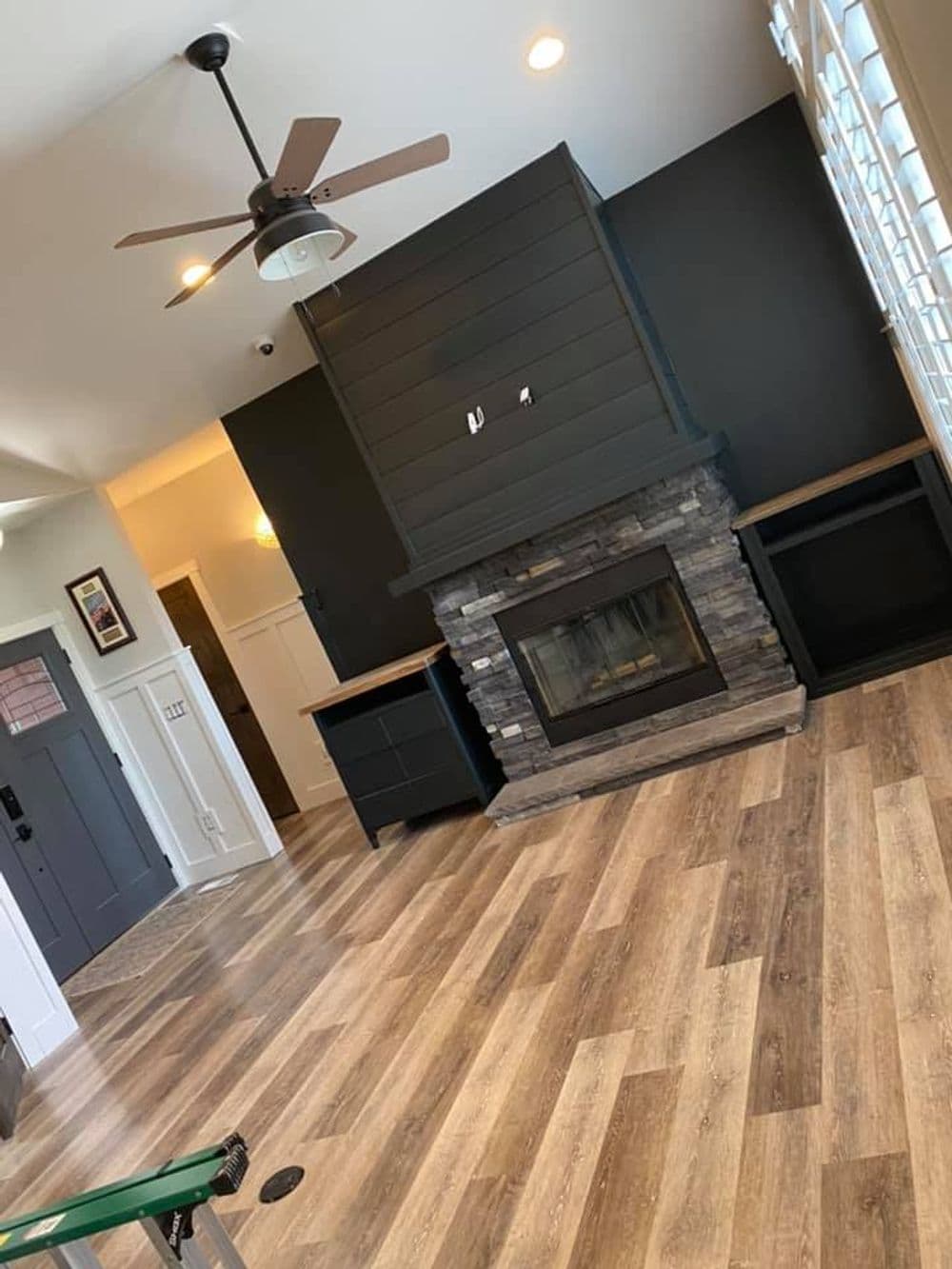 Modern living room with a stone fireplace, dark accent wall, and wooden flooring.