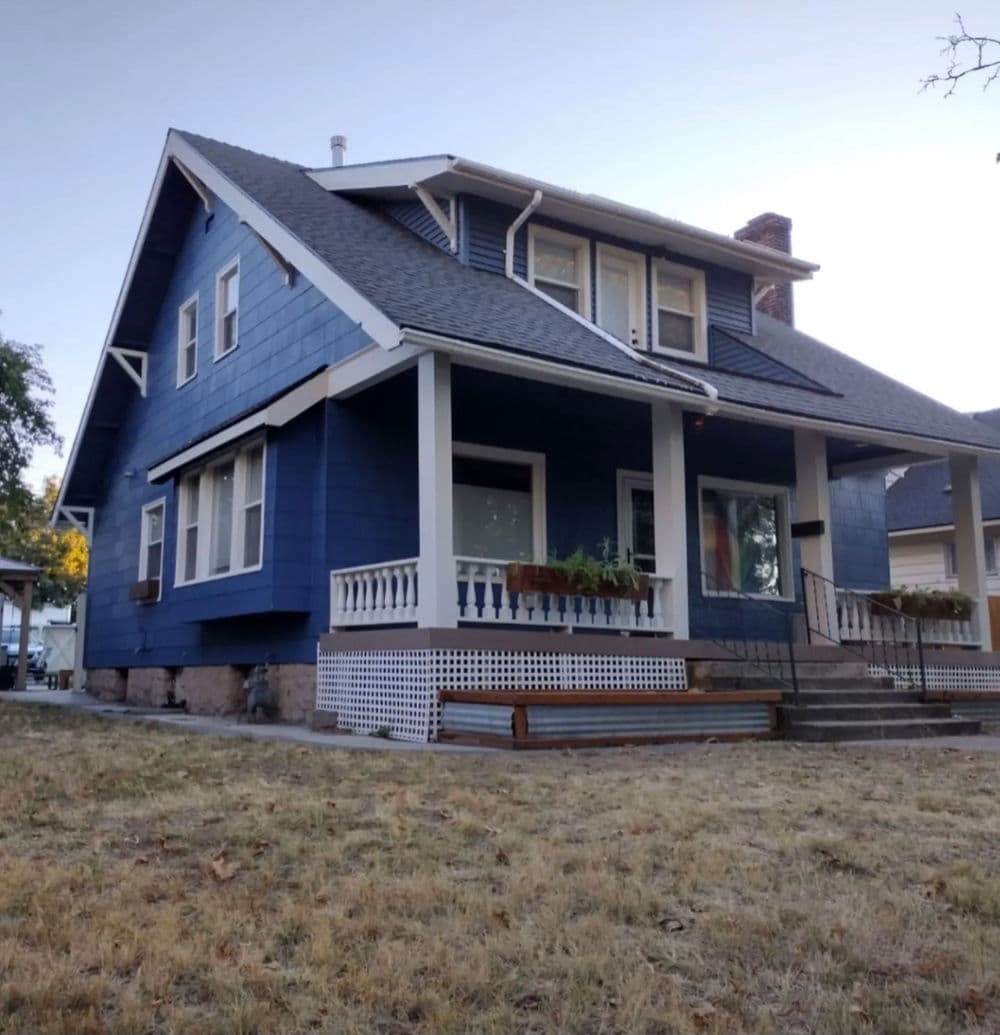 Blue craftsman-style house with a porch and garden, set in a grassy yard.