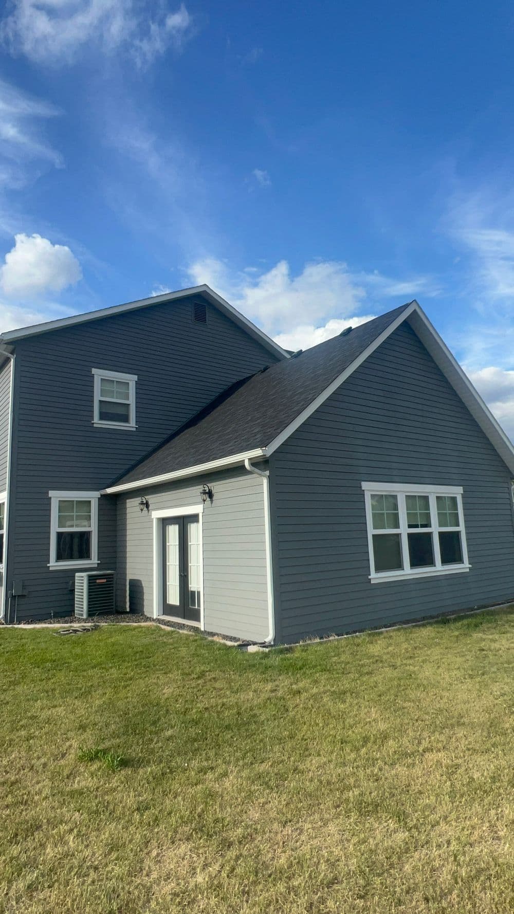 Modern gray house with large windows and a lawn under a blue sky. Ideal for family living.