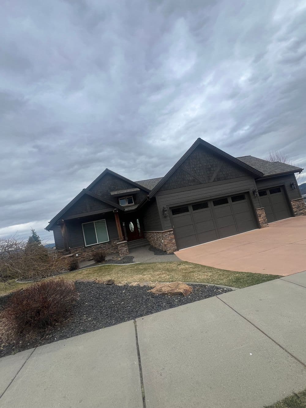 Modern brown house with stone accents, double garage, landscaped yard, and cloudy sky.