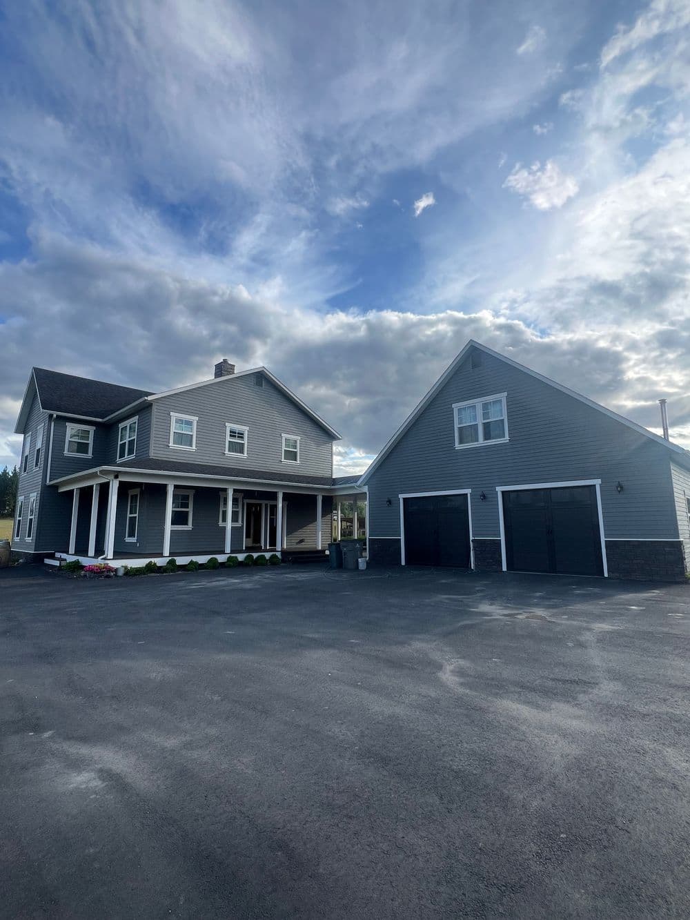Modern gray house with garage under a cloudy sky, showcasing a spacious driveway and landscaping.