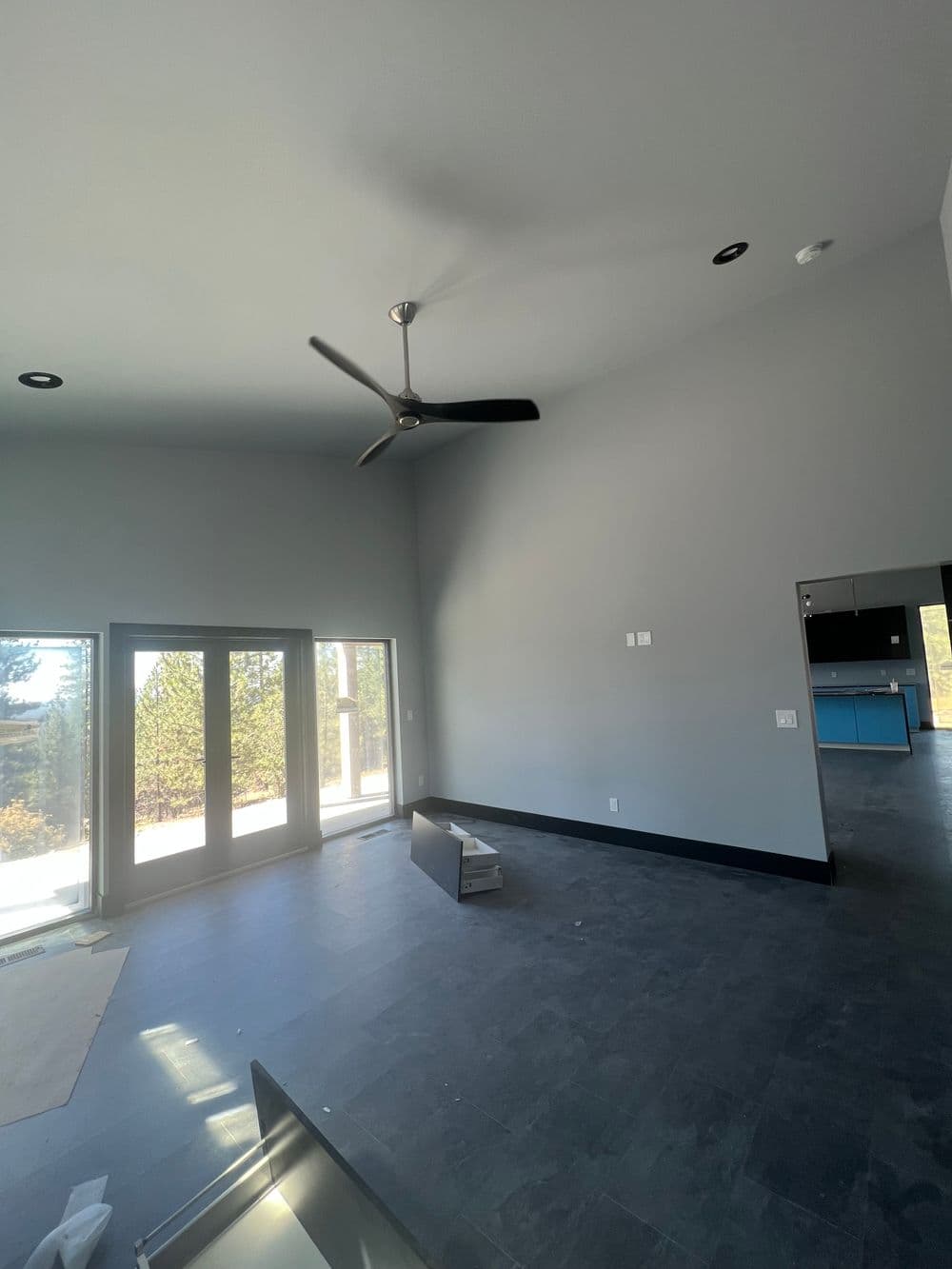 Modern living room with high ceilings, large windows, and sleek ceiling fan.