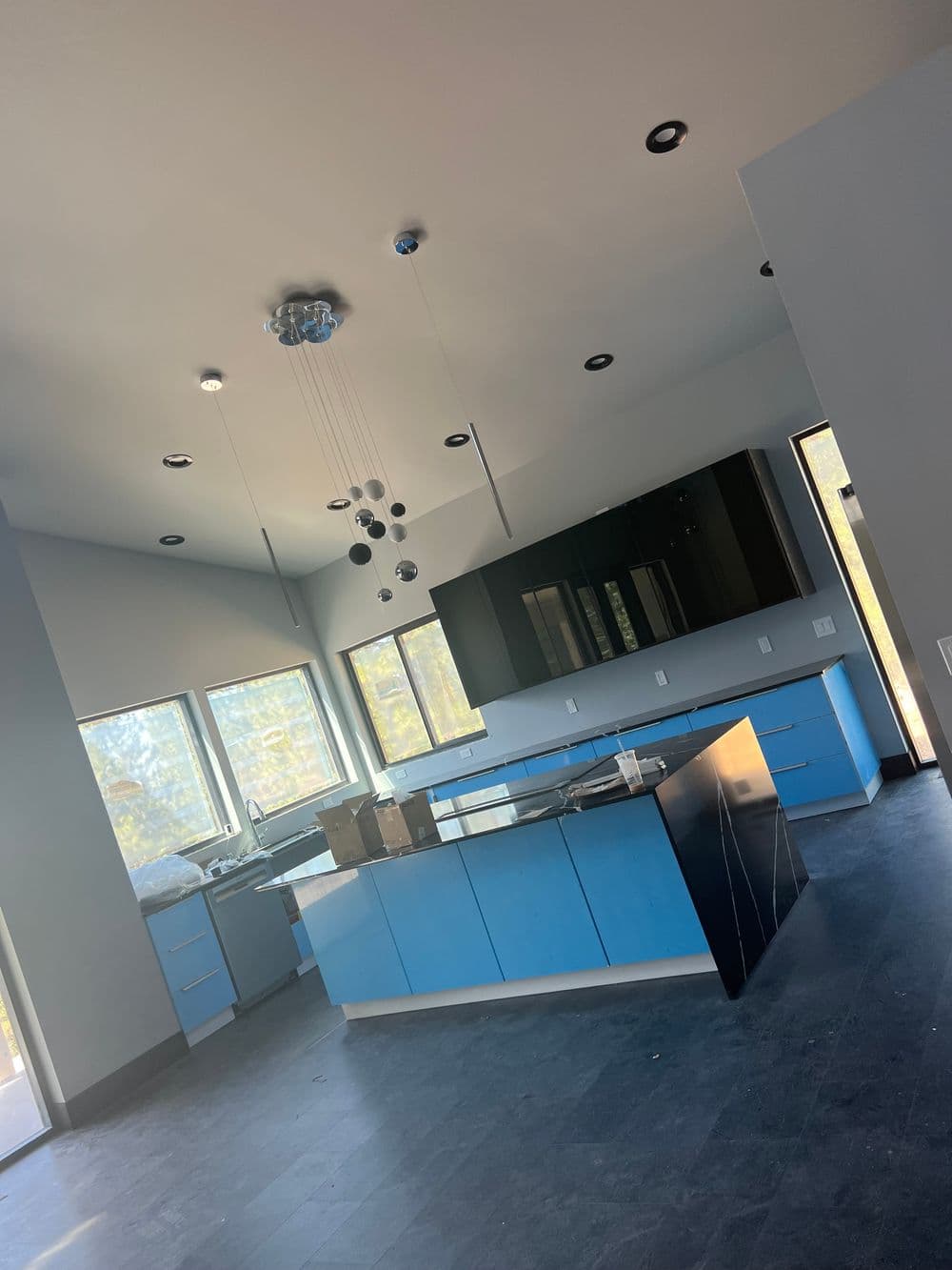 Modern kitchen with blue cabinetry, open layout, large windows, and stylish pendant lighting.