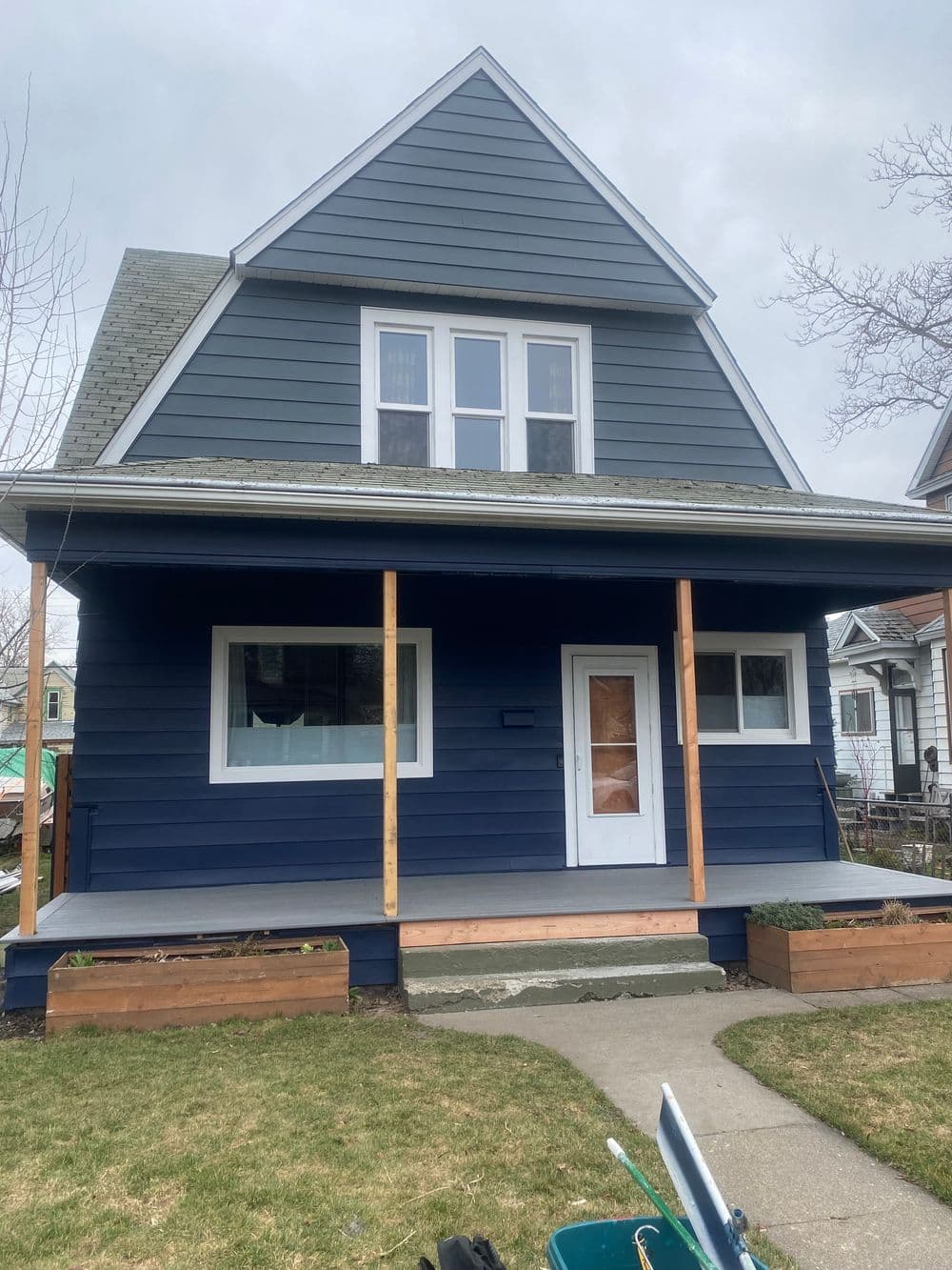Blue two-story house with porch and modern design, surrounded by green lawn and garden beds.