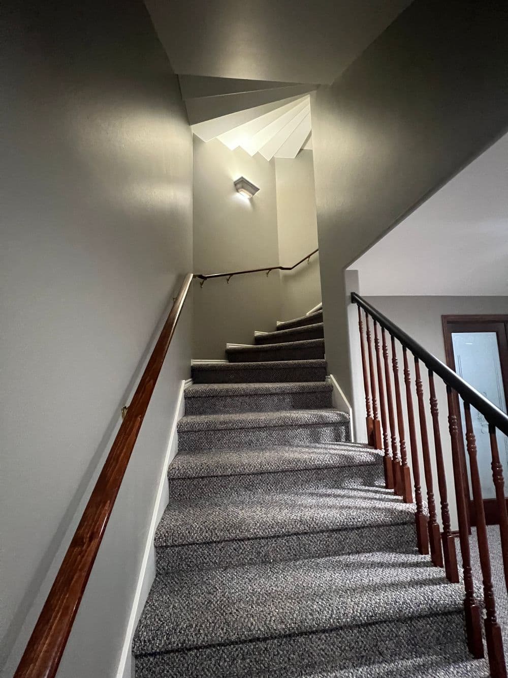 Staircase with carpeted steps, grey walls, and a light fixture illuminating the ascent.
