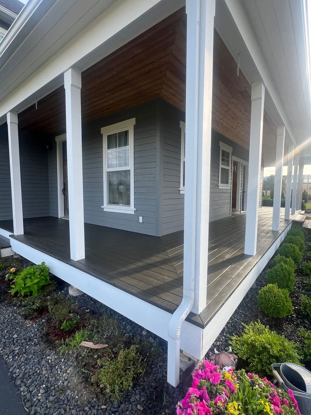 Modern gray house with a spacious porch, featuring vibrant flowers and a well-maintained garden.