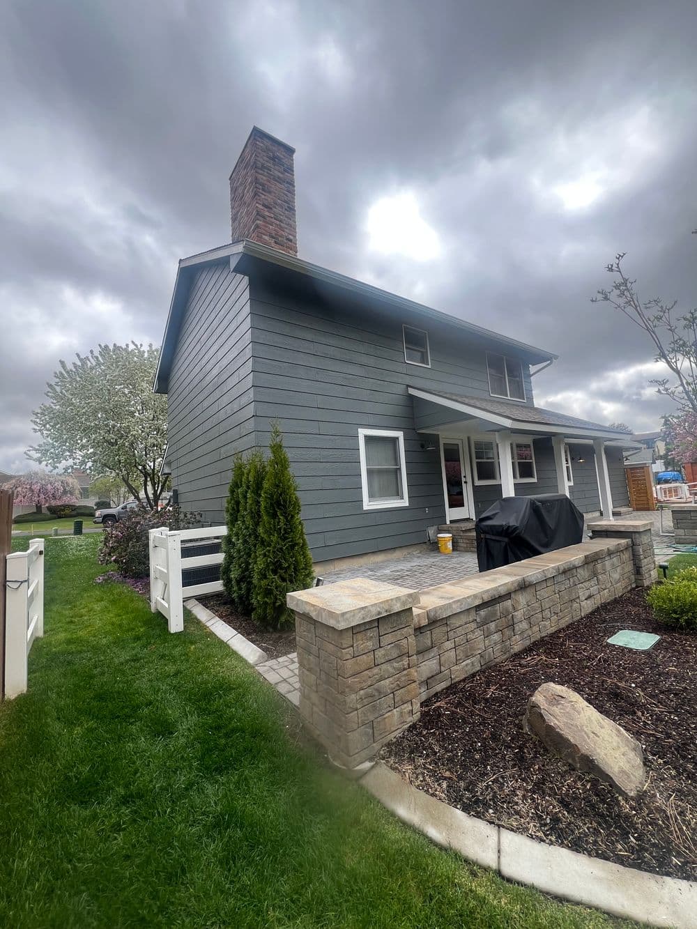 Modern gray house with stone accents, chimney, and well-maintained garden landscaping.