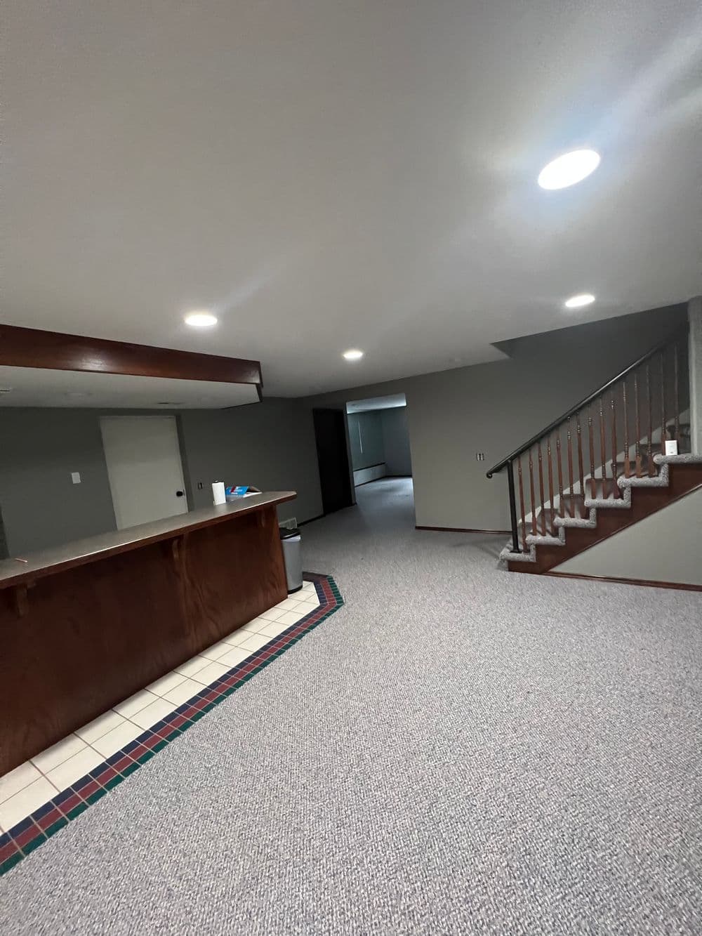 Basement interior with carpet, bar area, and staircase leading to upper floors. Bright lighting.