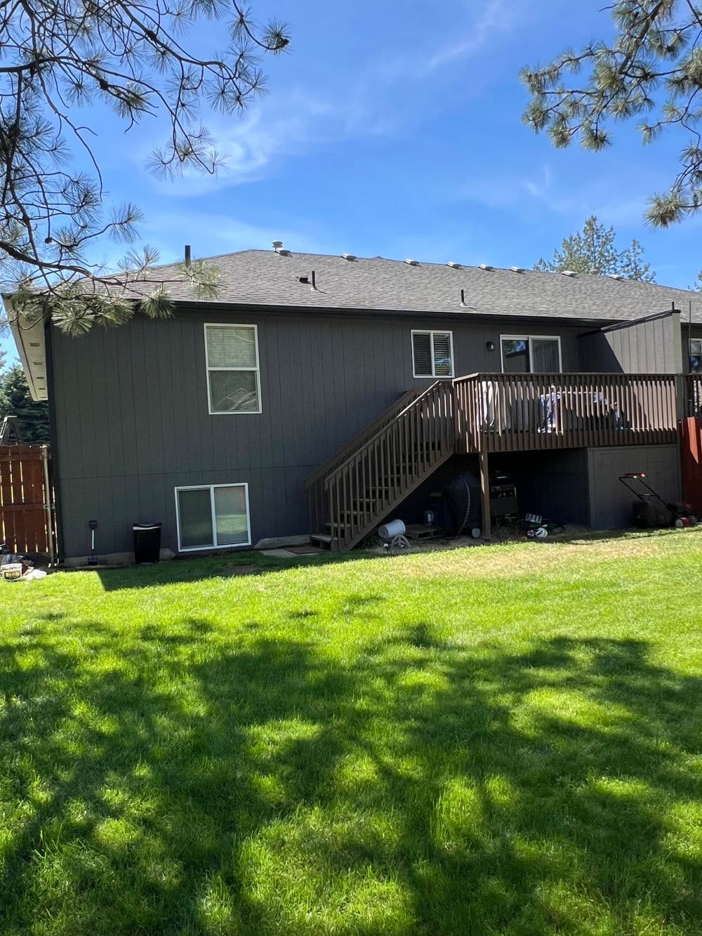 Back view of a modern home with a deck, surrounded by green grass and trees. Clear blue sky.