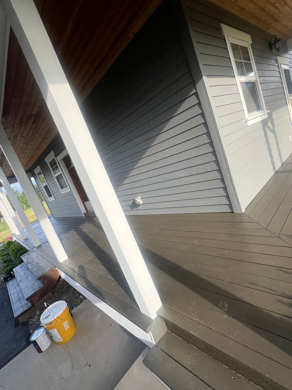 Modern home exterior with gray siding, white trim, and wooden deck in natural light.