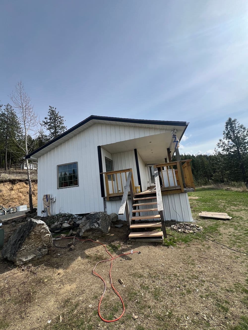 Small white cabin with wooden porch, surrounded by trees and grassy area. Ideal for nature retreats.