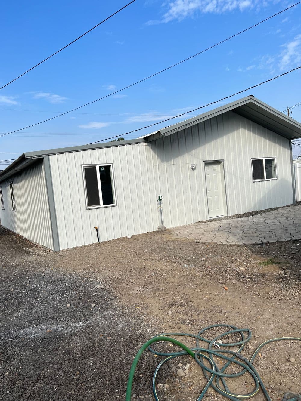 Newly constructed metal-clad house with windows, door, and gravel driveway outdoors.