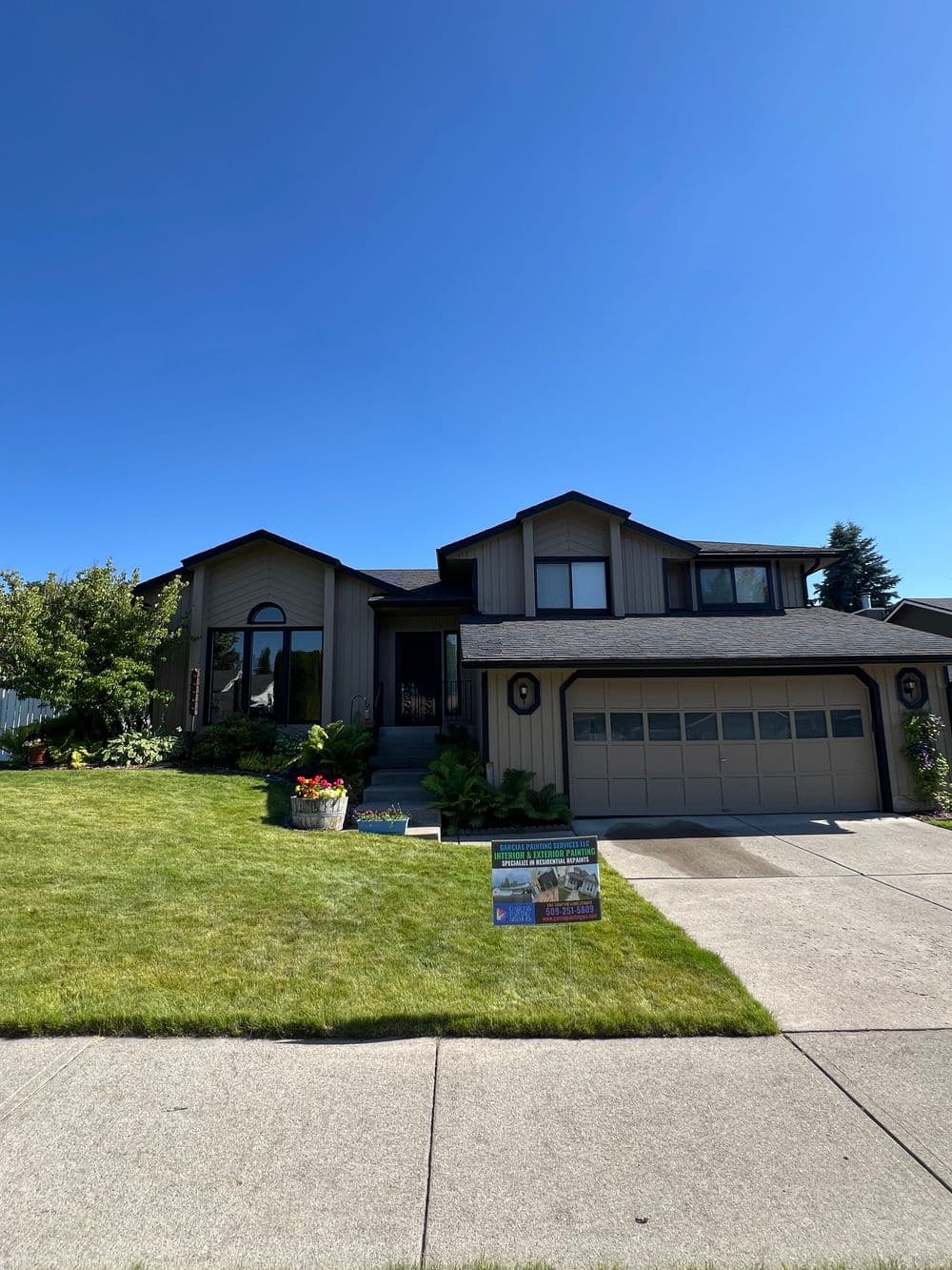 Modern suburban home with landscaped yard and garage on a sunny day. For sale sign in front.