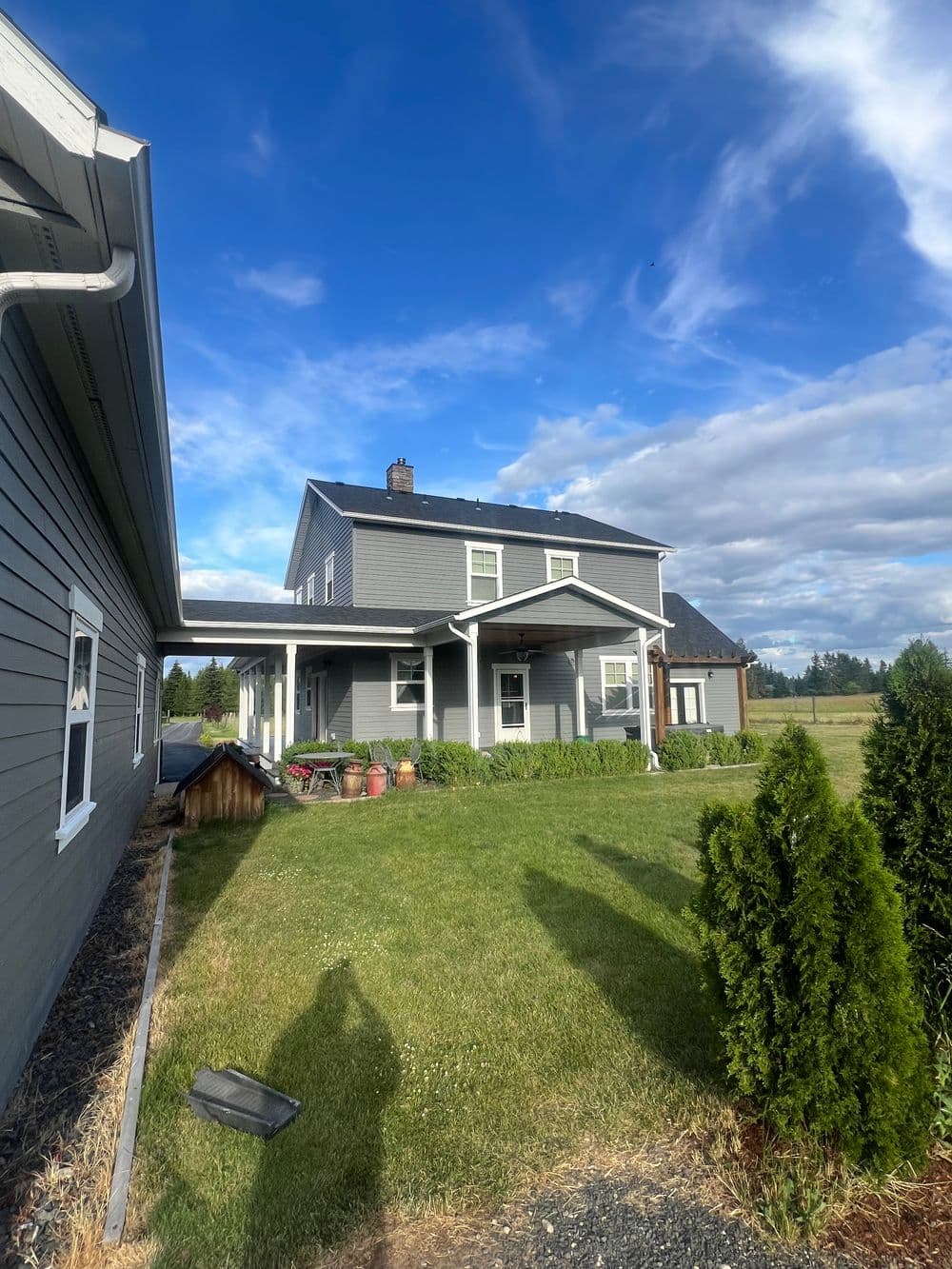 Two-story gray house with a front porch, green lawn, and blue sky in the background.