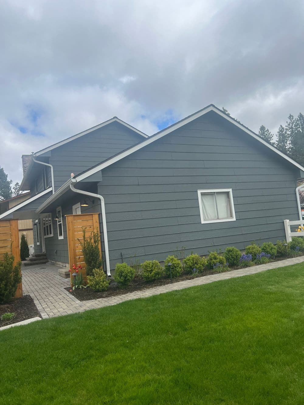 Modern gray house with a neatly landscaped yard and pathway on a cloudy day.