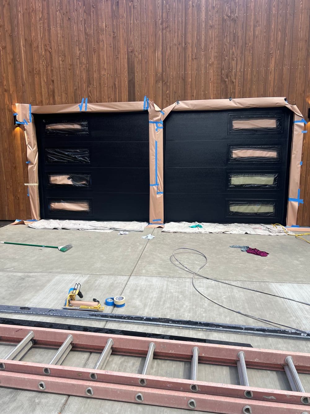 Black garage door with modern design, under construction, taped for painting.
