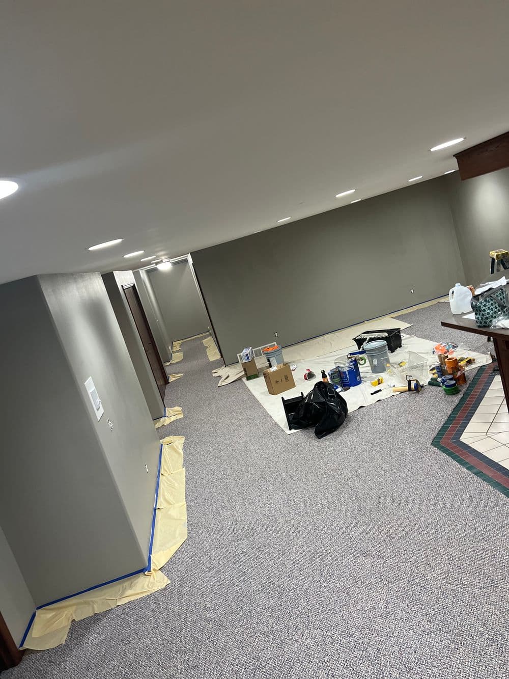 Renovated basement with gray walls, newly laid carpet, and painting supplies scattered.