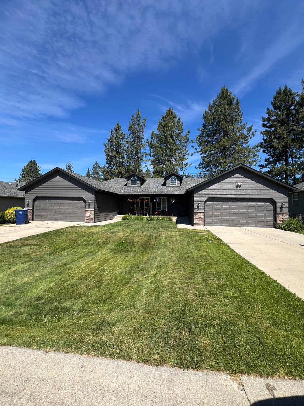 Gray split-level house with two garages, surrounded by a well-kept lawn and tall trees.