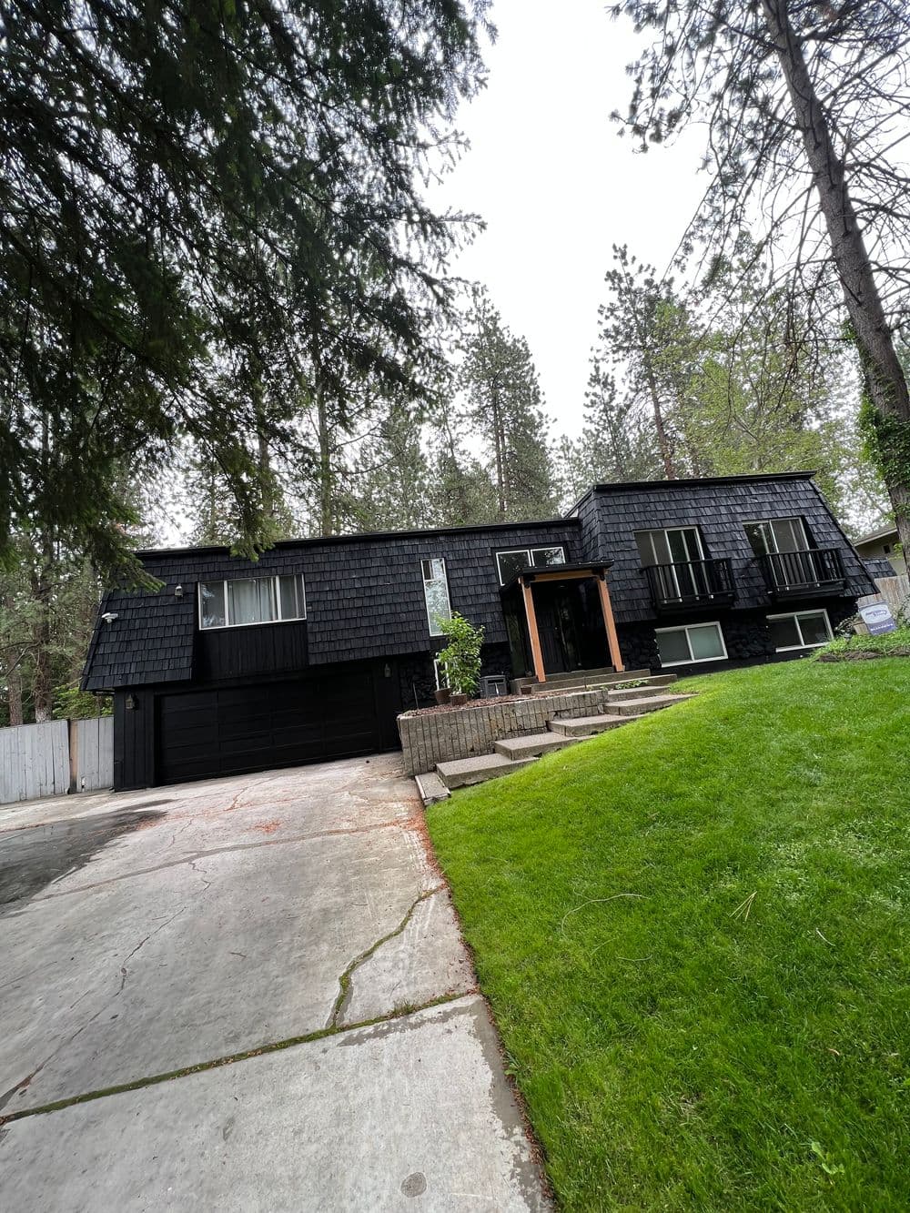 Modern black house with a sloped roof, large windows, and a manicured lawn surrounded by trees.
